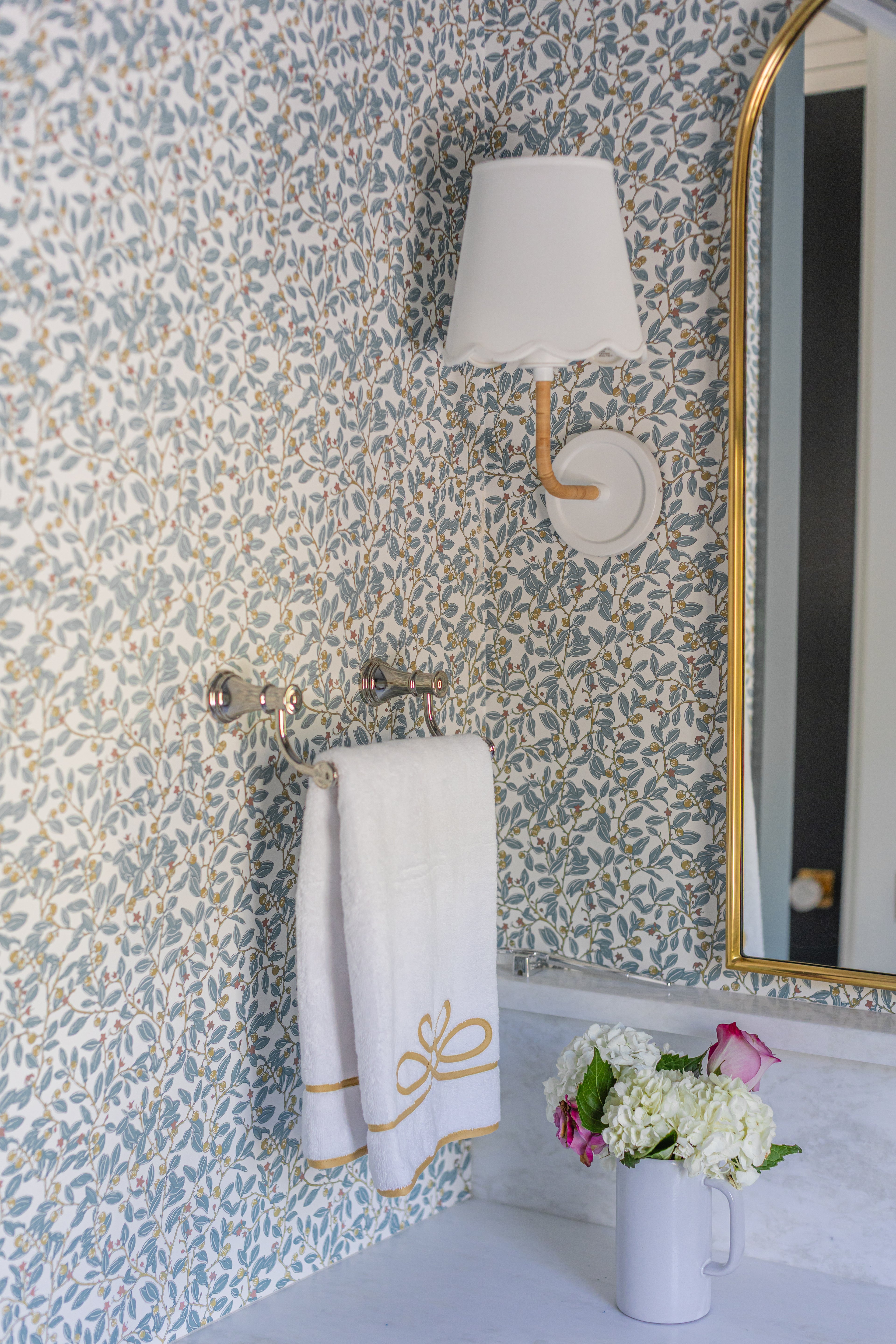 Blue Limes Wallpaper with a subtle leaf and berry pattern, featuring a white sconce, towel rack, and mirror.