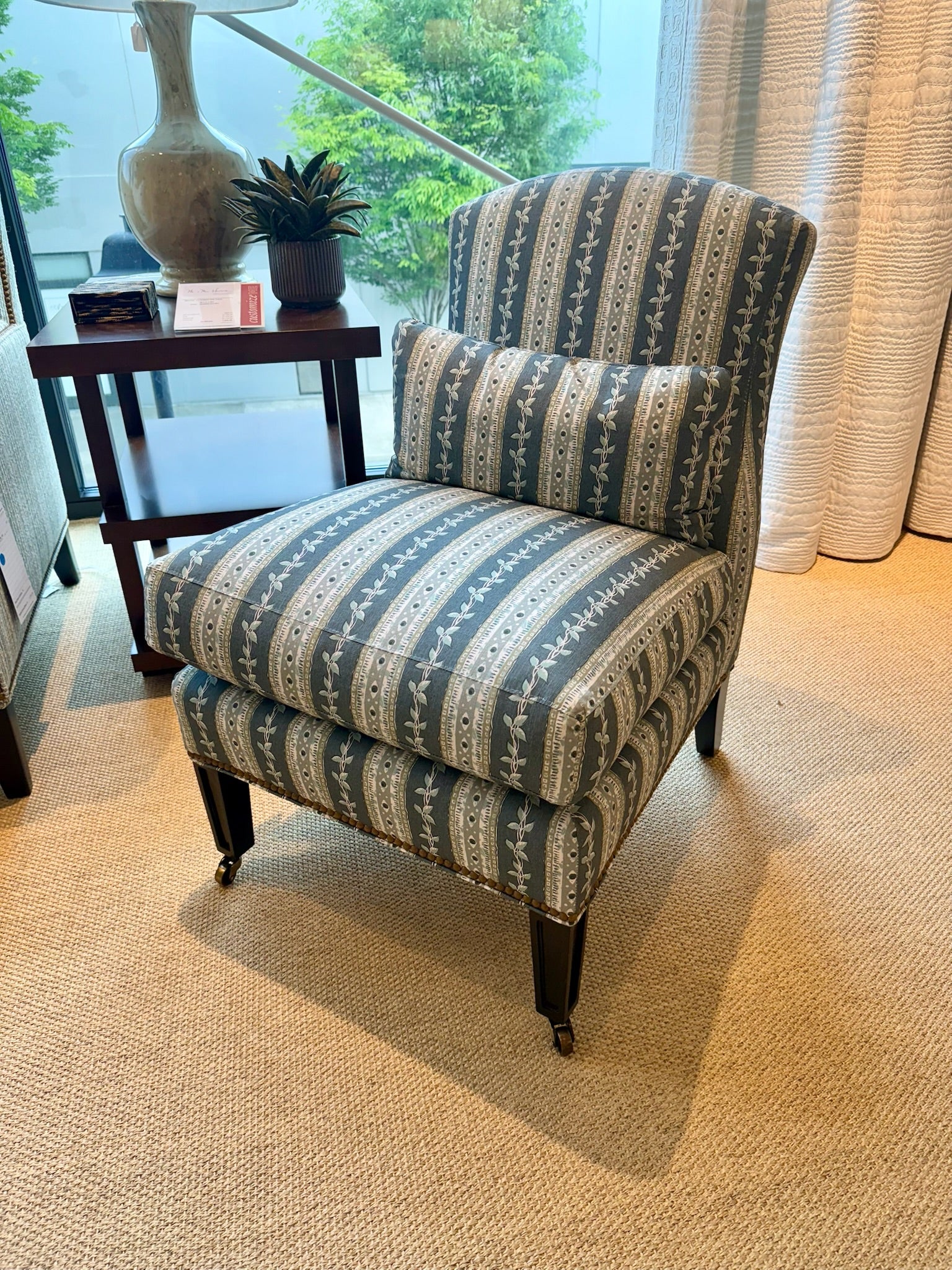 Upholstered slipper chair in Trellis Fabric Marine, featuring blue and white stripes with a delicate leaf pattern.