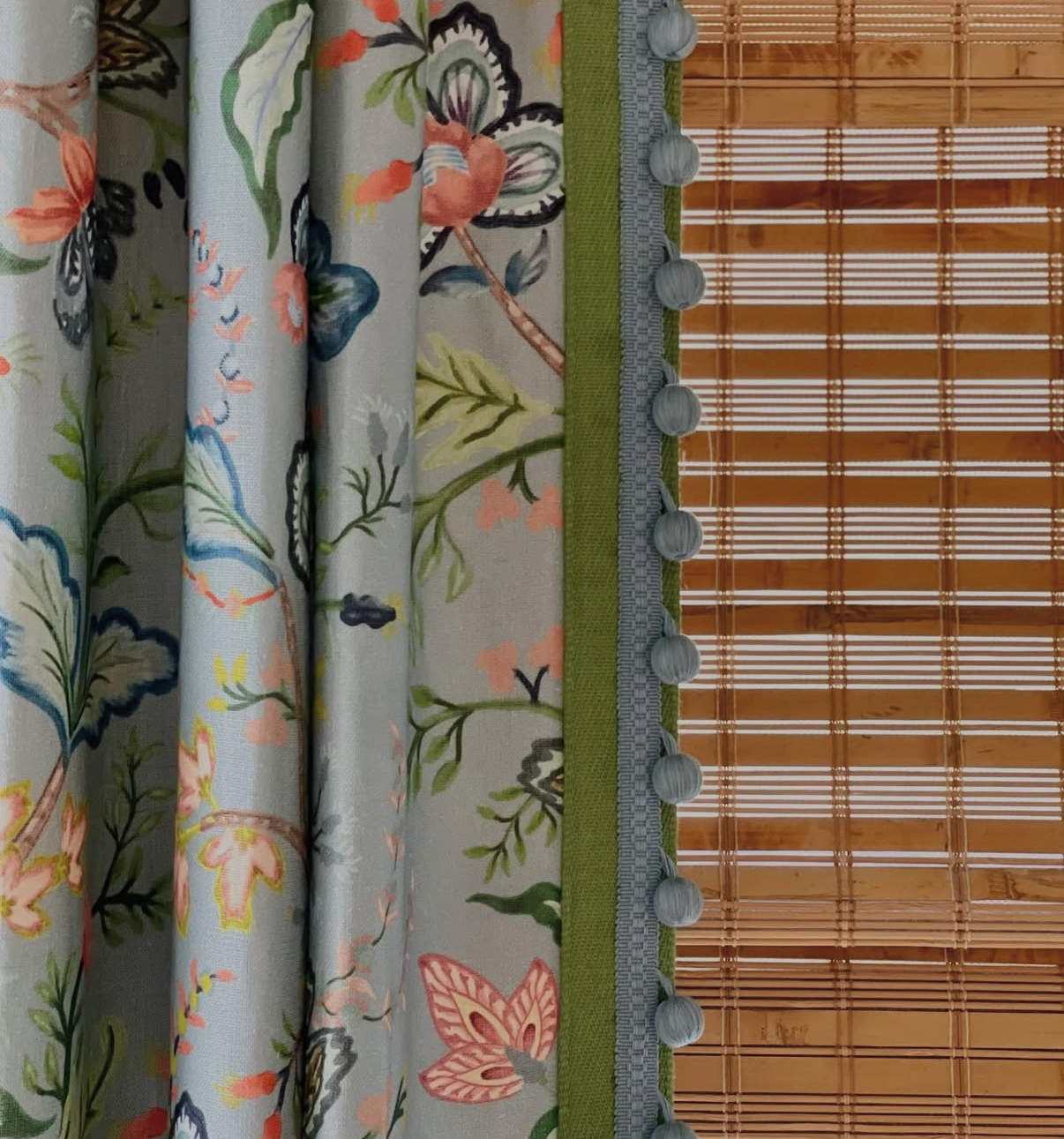 Vera Vine Fabric in House Blue, a floral Belgian linen curtain with green trim and blue pom-pom fringe, next to a bamboo blind.