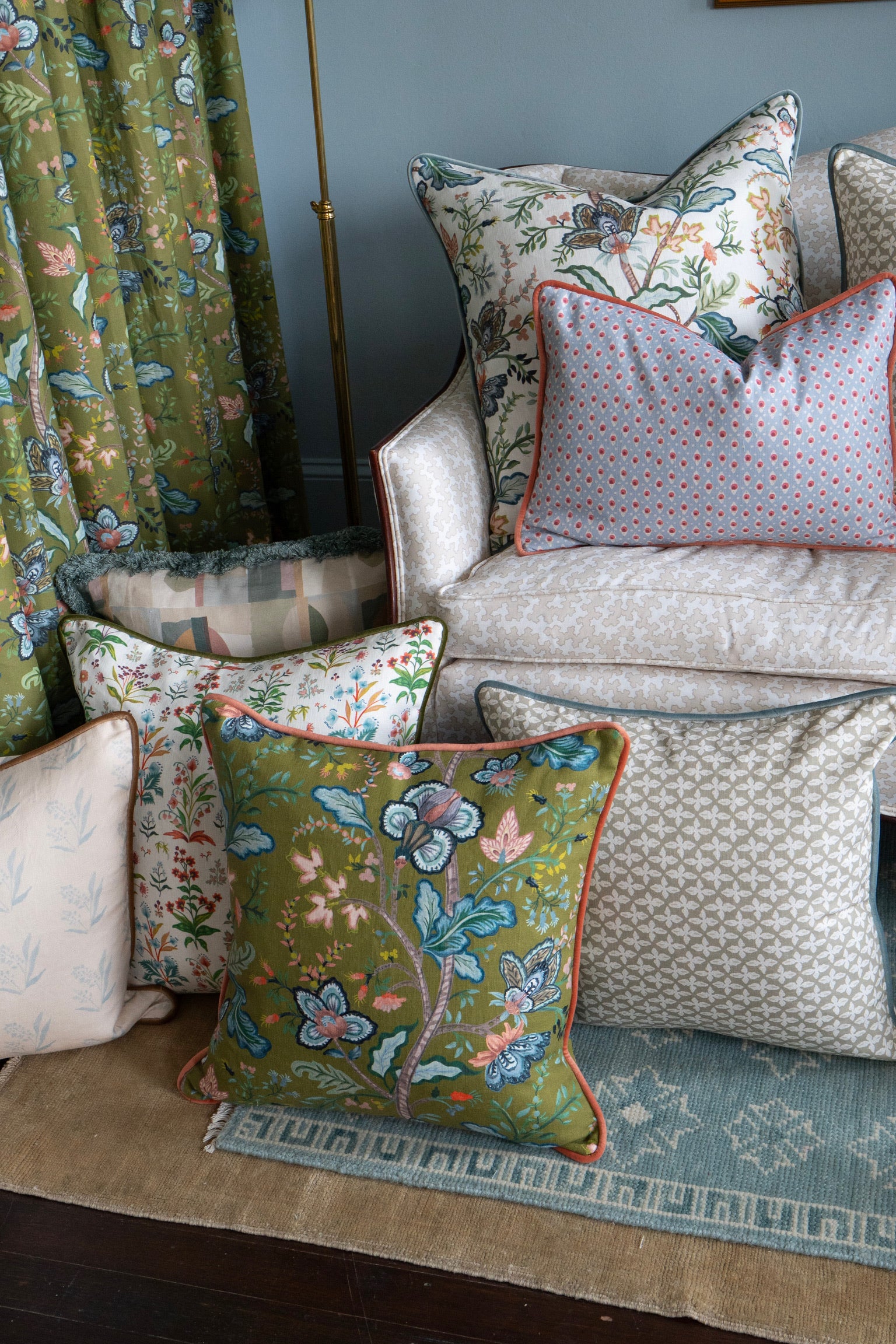 Linen Vera Vine Leaf pillow in olive green with floral design, surrounded by other patterned pillows and curtains.