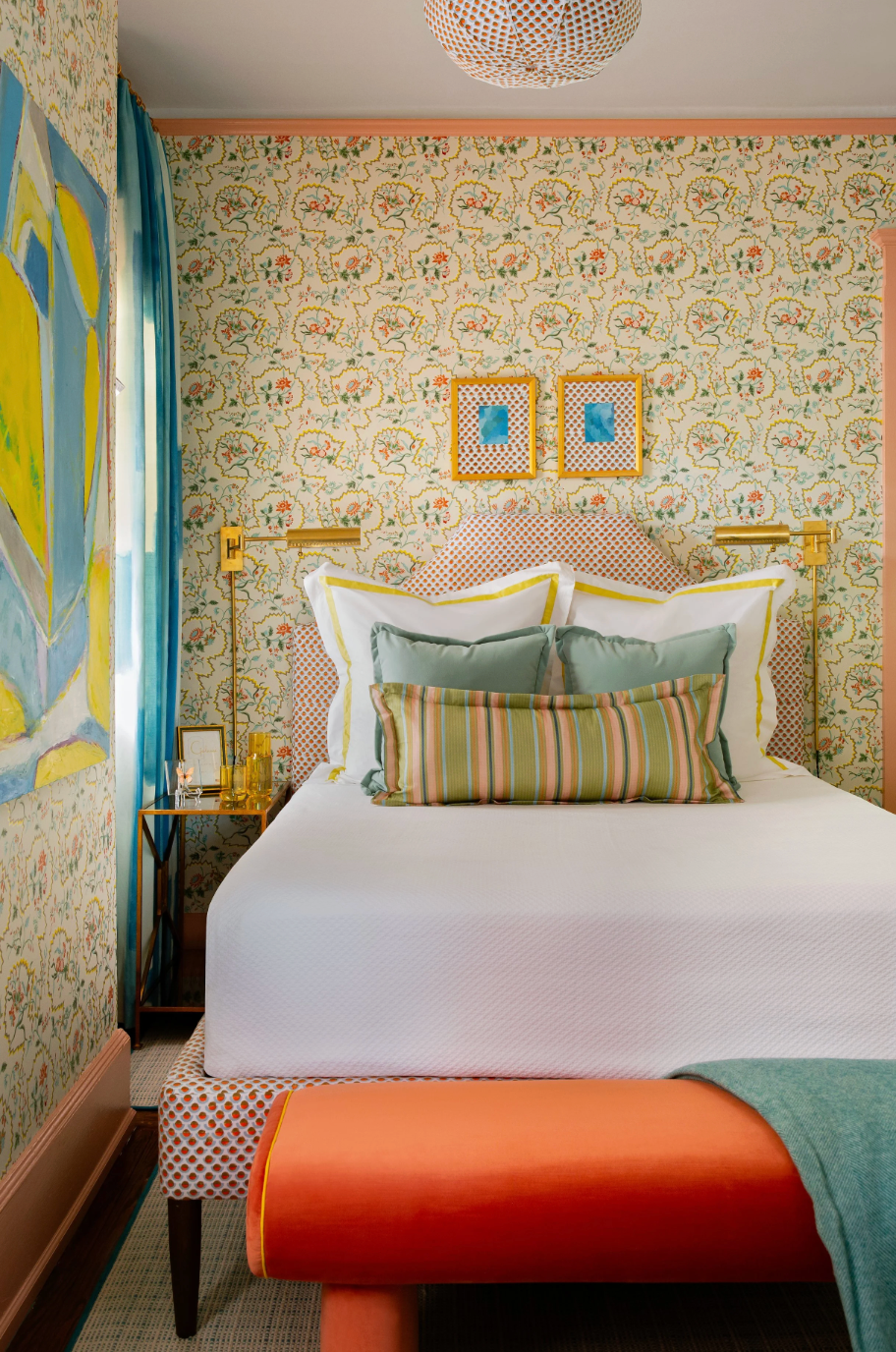Wentworth Multi fabric wallpaper with a bed featuring a patterned headboard, white bedding, and an orange bench.
