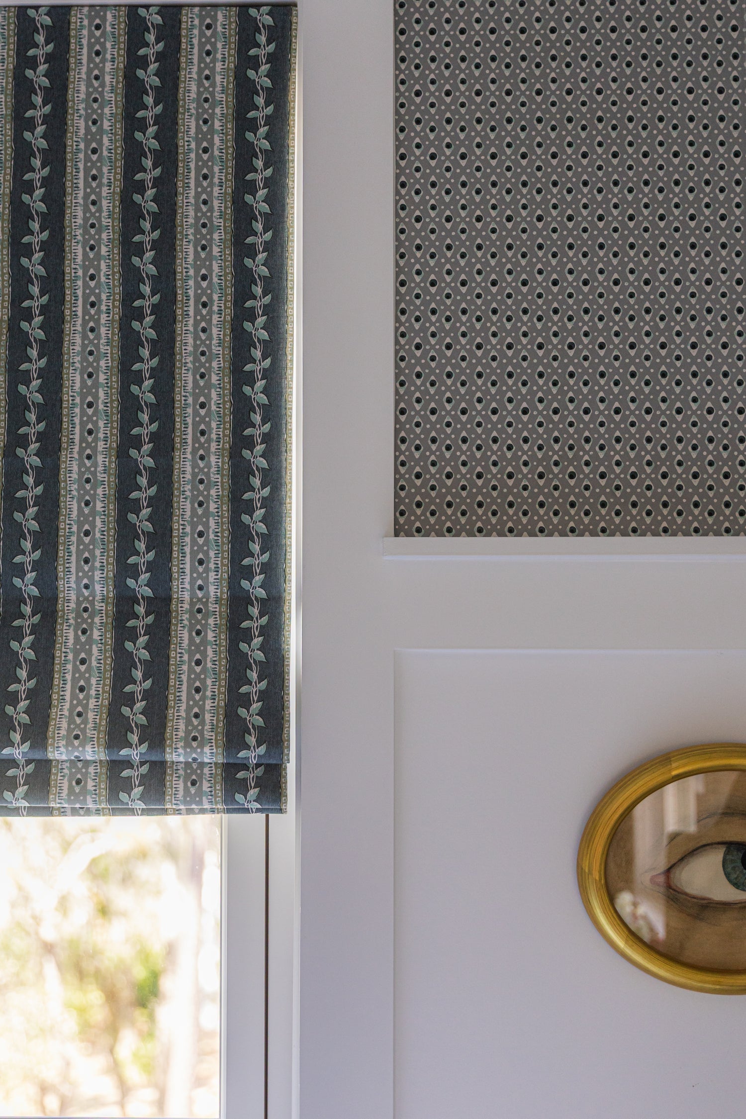 Della Dot Marine wallpaper with a small geometric pattern, paired with a striped botanical roman shade.
