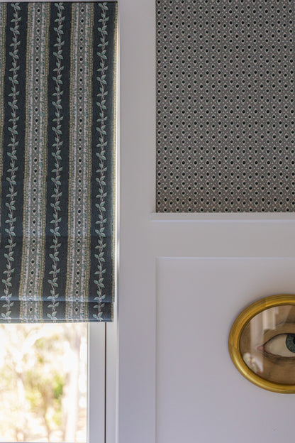 Della Dot Marine wallpaper with a small geometric pattern, paired with a striped botanical roman shade.
