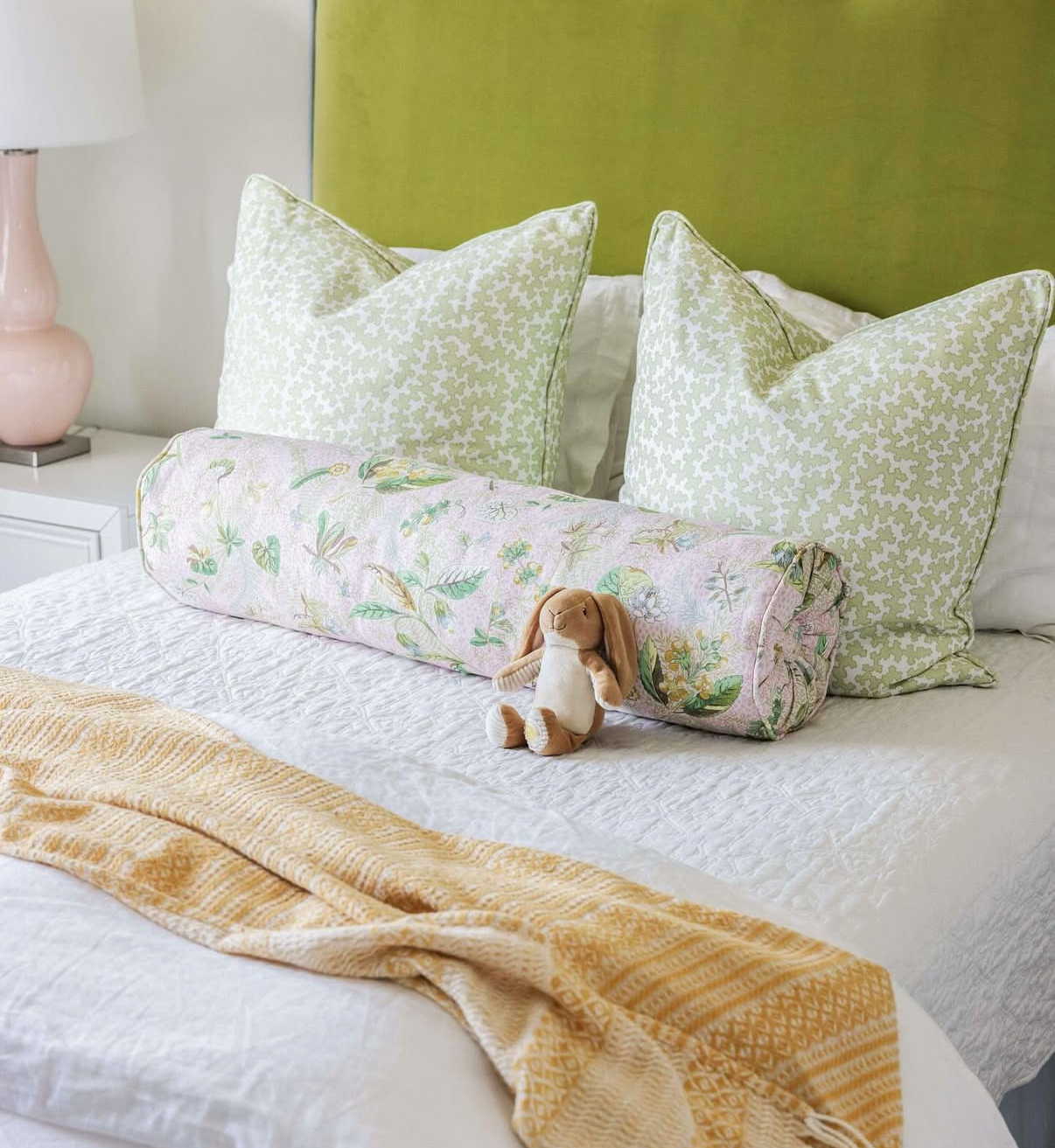 Dover Fabric - Apple: Pink botanical bolster pillow and green patterned square pillows on a bed.