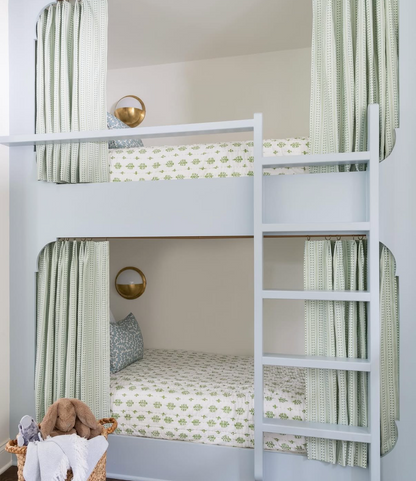 Light blue bunk beds with green and white botanical print bedding and privacy curtains.