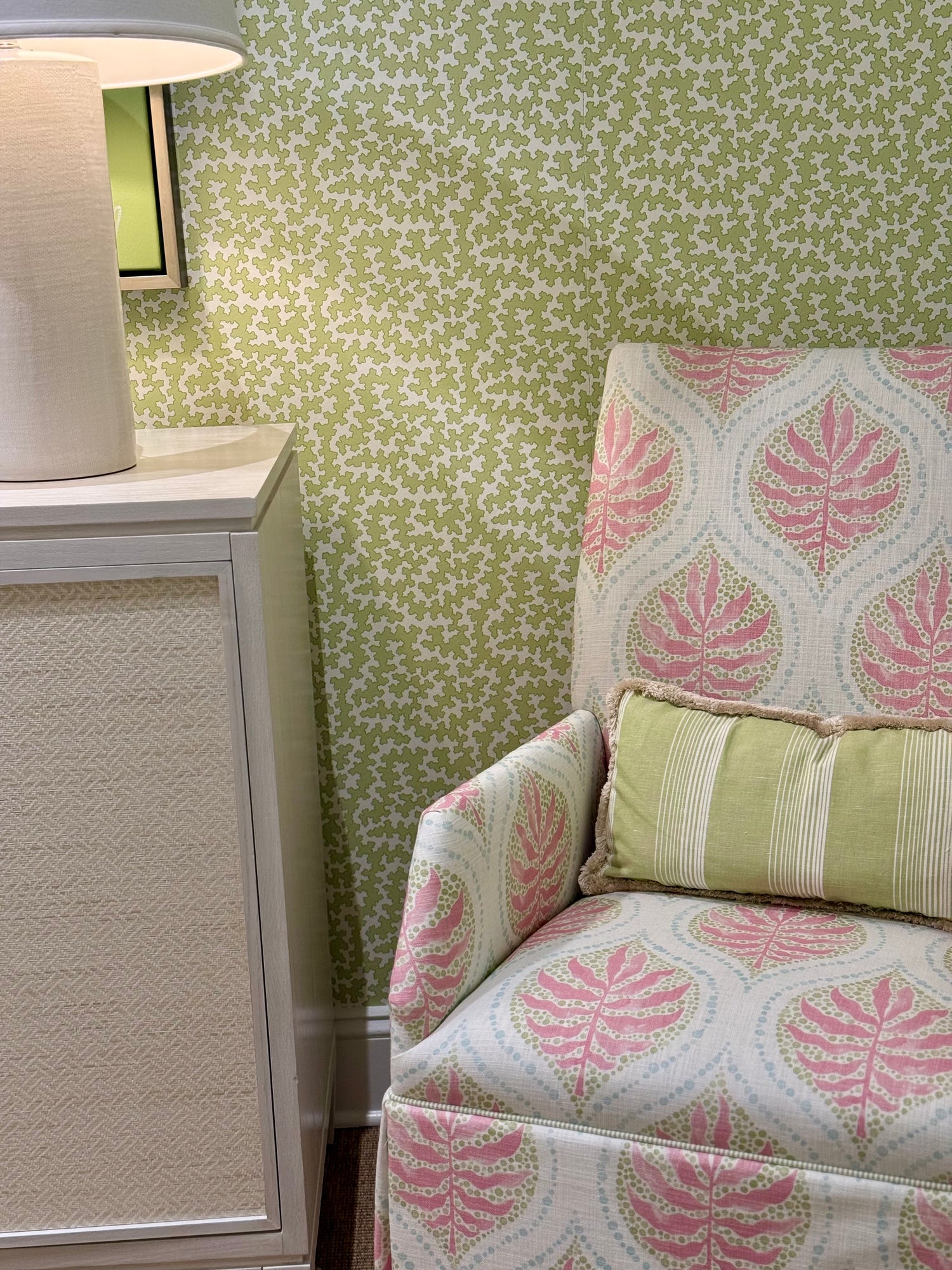 Dover Apple green patterned wallpaper behind a pink and white leaf print armchair with a striped pillow.