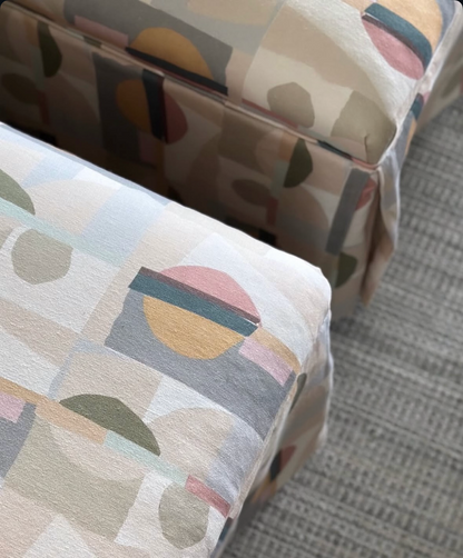 EH x Renee Bouchon Kipsy multi-color abstract linen fabric on two upholstered ottomans.