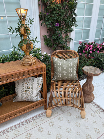 Rattan furniture set with two decorative pillows featuring floral patterns. One pillow is olive green, the other beige.