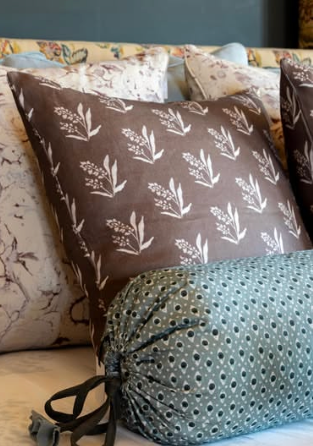 Brown linen pillow with white floral pattern and a teal bolster pillow with small white dots.