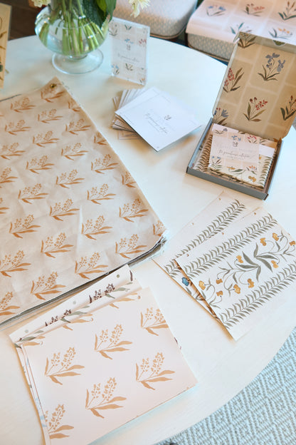 Marigold Marbella wallpaper yardage with a repeating floral pattern, alongside coordinating samples and stationery.