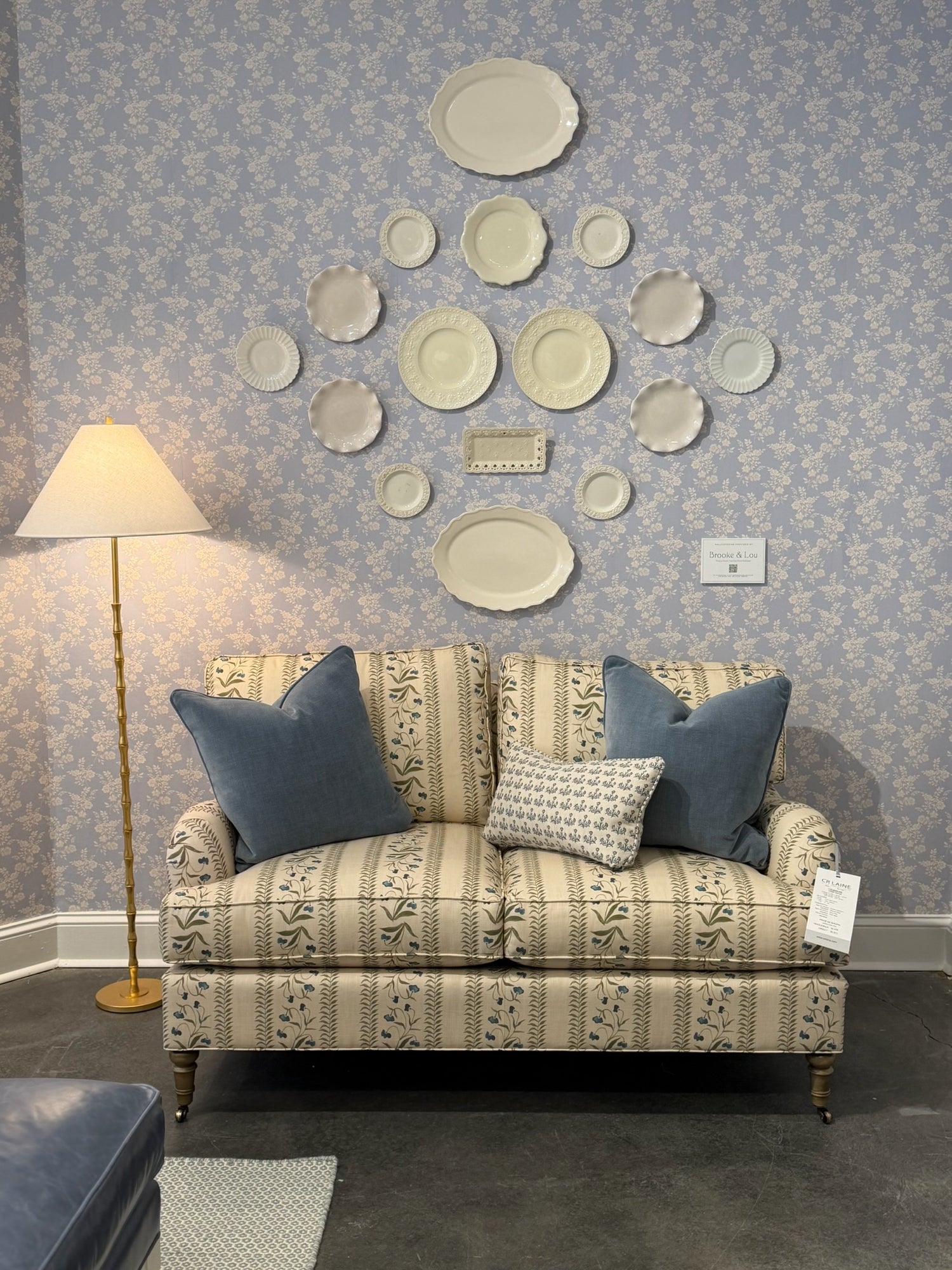 EH x Renee Bouchon Tula Lapis linen fabric on a sofa with blue pillows, against a floral wallpaper.