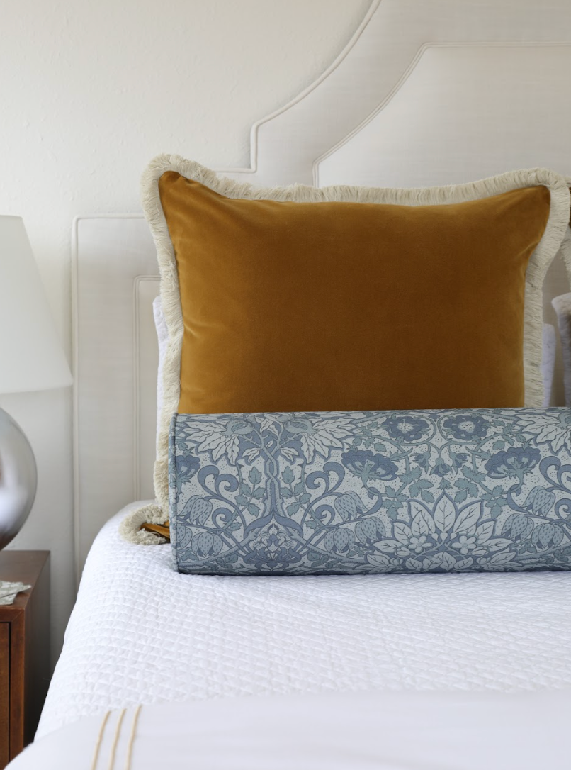 Cobalt Flora Fabric bolster pillow with a botanical pattern, paired with a mustard velvet pillow on a white bed.