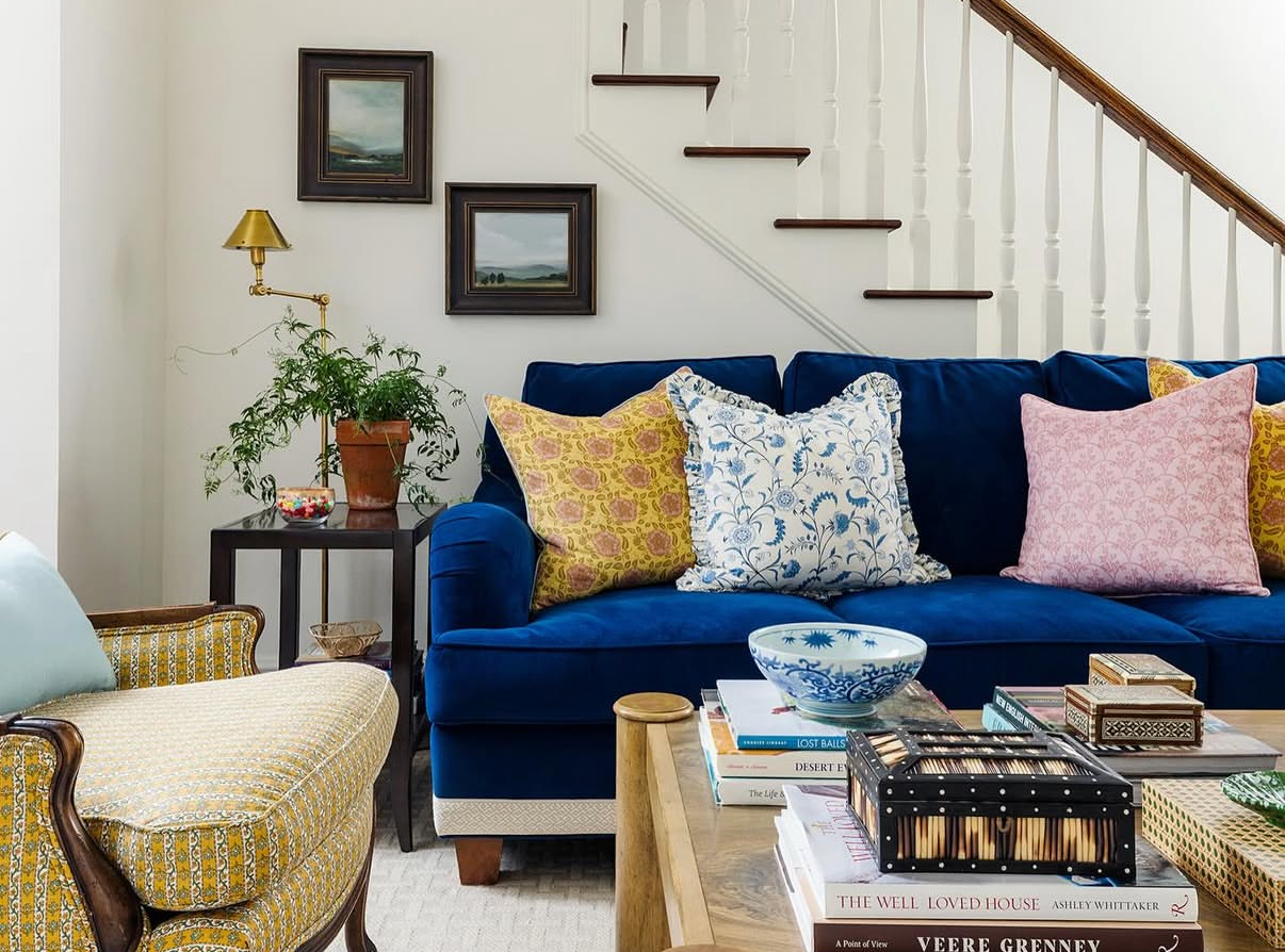 Laurel Fabric - Poppy on a blue velvet sofa with yellow, blue, and pink floral pillows.