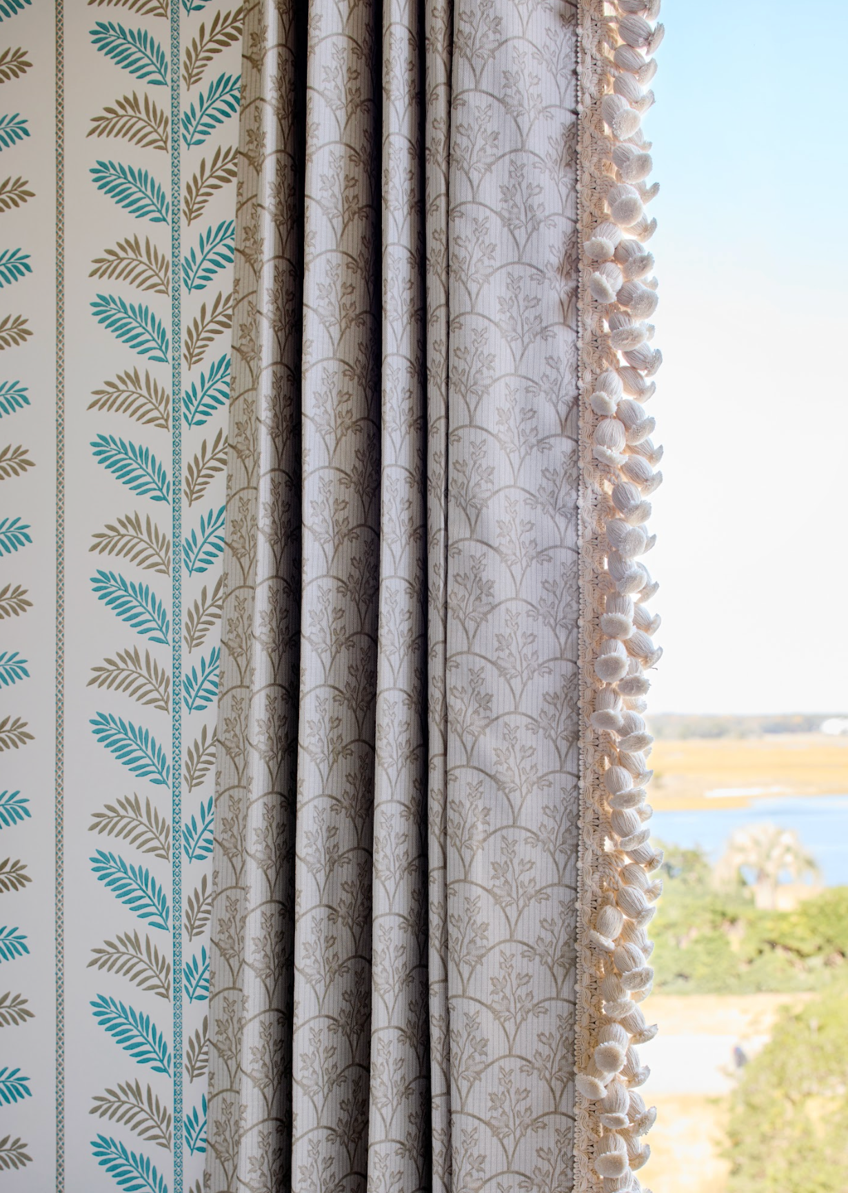 Laurel Fabric in Putty, a linen-cotton blend with a delicate leaf pattern, used as a curtain with decorative trim.