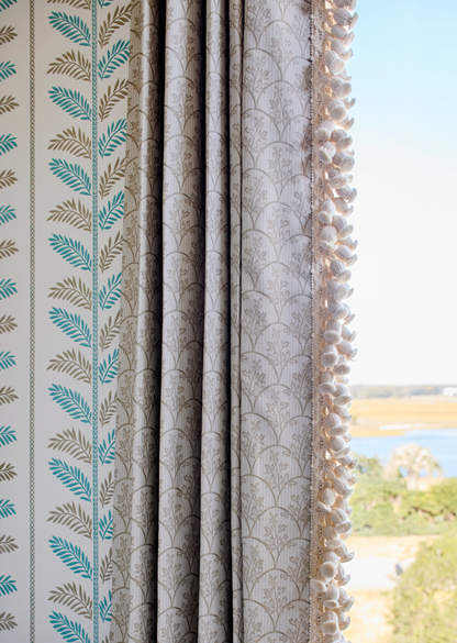 Laurel Fabric in Putty, a linen-cotton blend with a delicate leaf pattern, used as a curtain with decorative trim.