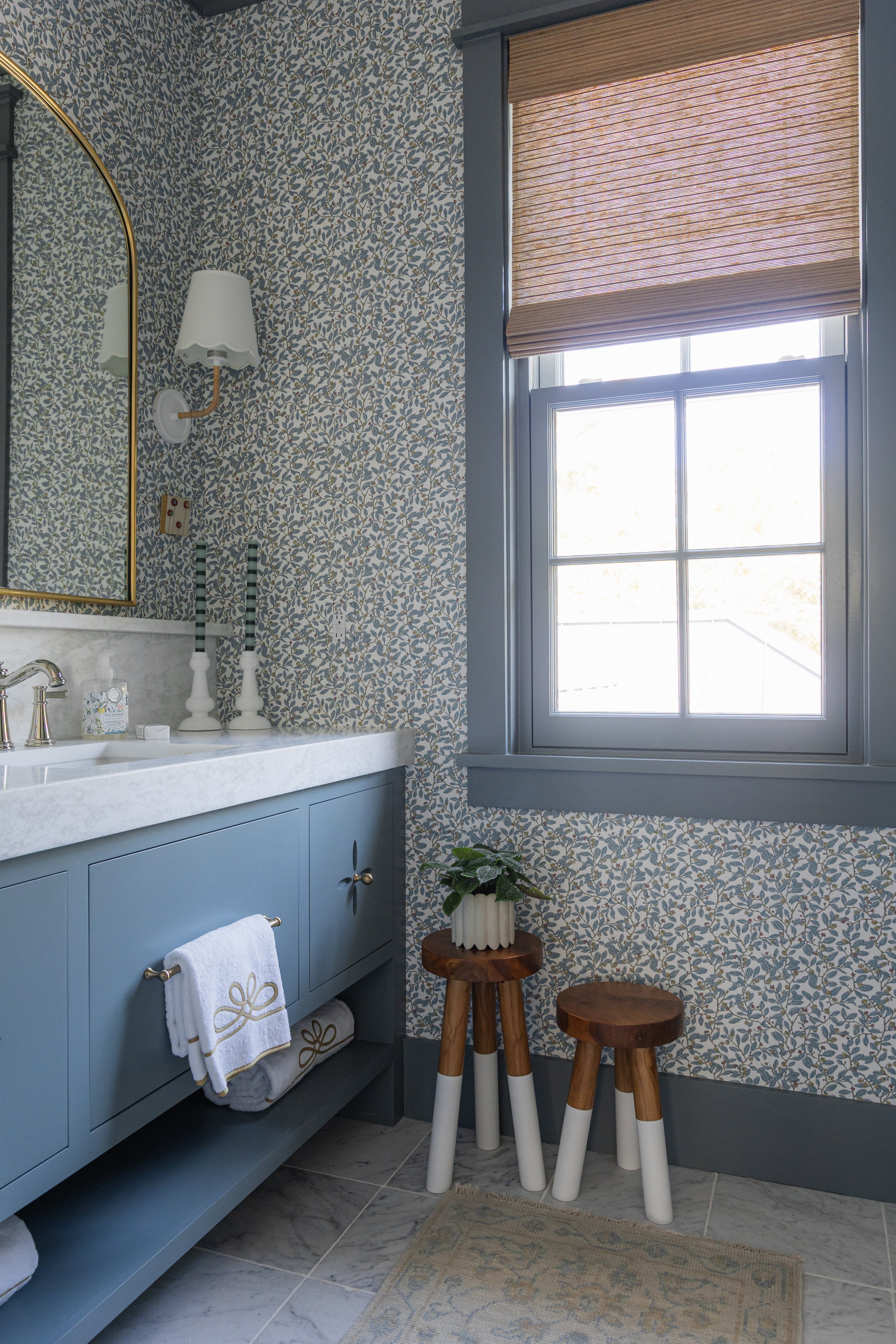 Blue Limes Wallpaper with a subtle leaf pattern in a stylish bathroom featuring a blue vanity and gold mirror.