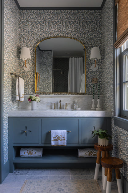 Blue Limes Wallpaper with a subtle floral pattern in a stylish bathroom featuring a vanity and gold mirror.