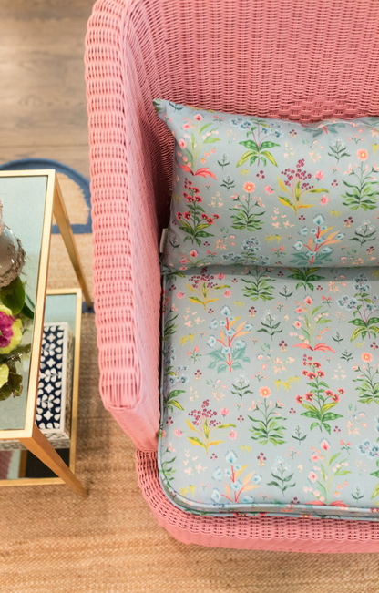 Pink wicker chair with Meadow Multi Fabric in House Blue, featuring a colorful floral pattern on Belgian Linen.