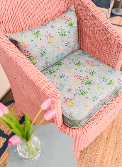 Pink wicker chair with Meadow Multi Fabric in House Blue, featuring a delicate floral pattern on Belgian Linen.