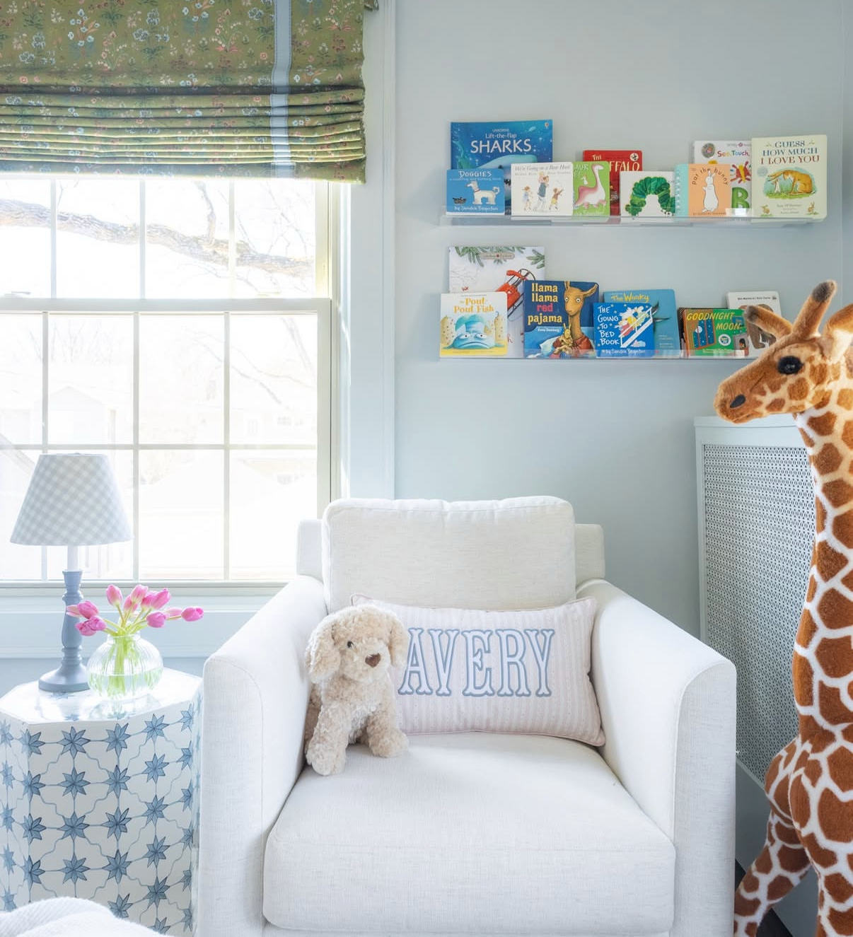 Nursery with white linen armchair, blue leaf fabric roman shade, and children&