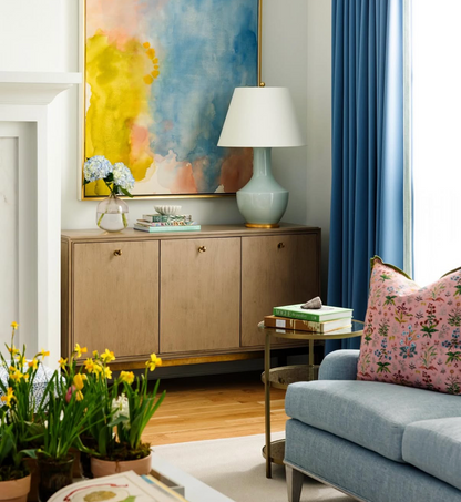 Pink floral "Petal" Meadow Multi fabric pillow on a blue sofa in a bright living room.
