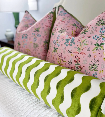 Pink floral linen pillows with green trim and a green and white wavy bolster pillow on a white bed.