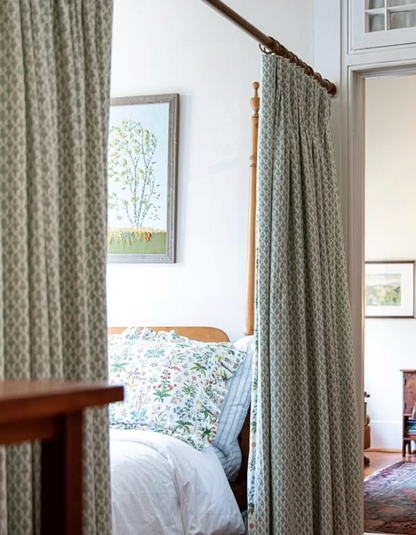 White Meadow Multi Fabric curtains with a subtle green geometric pattern, framing a wooden bed.