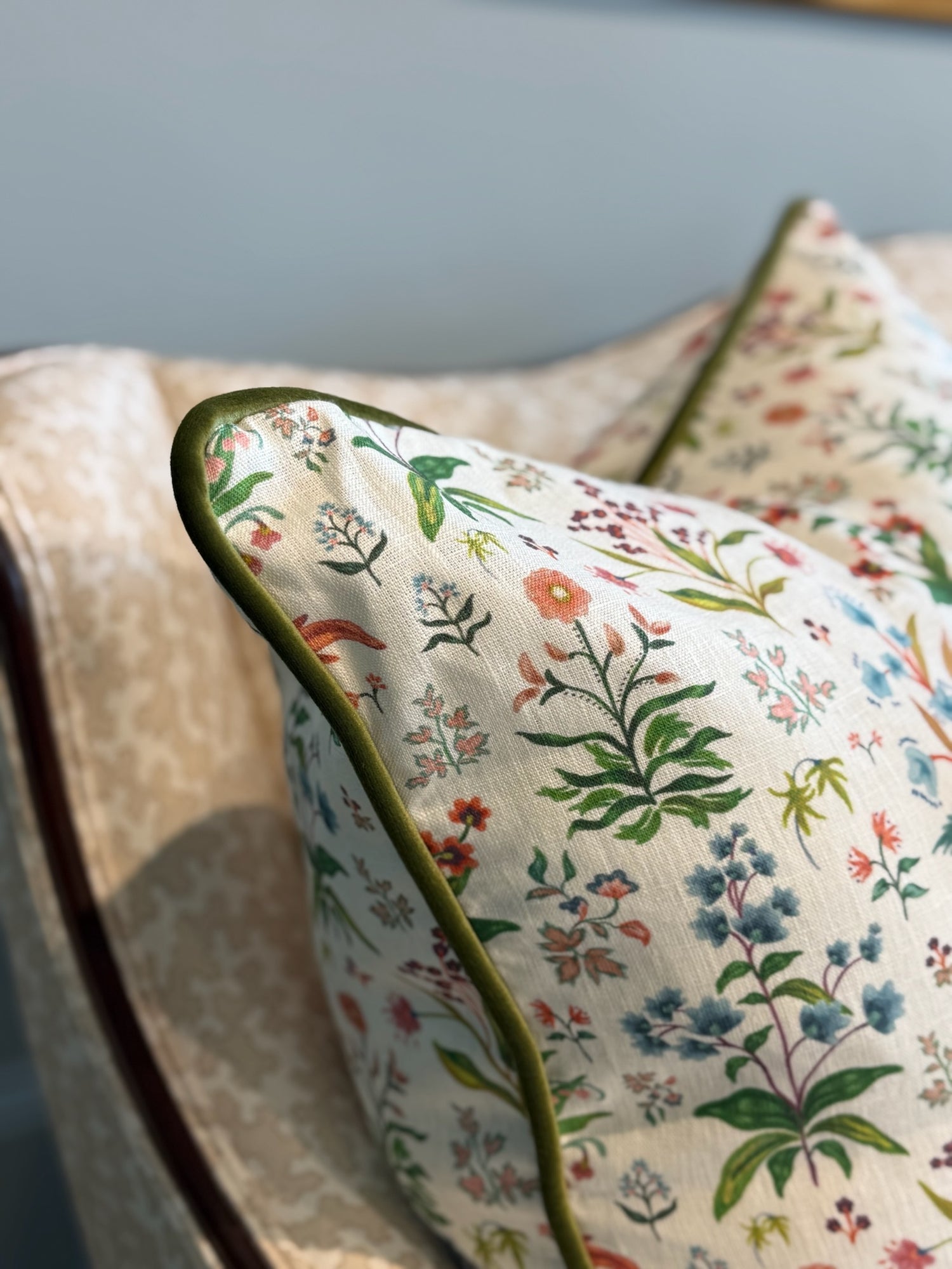 White linen Meadow Multi Pillow with colorful floral print and green piping on a sofa.