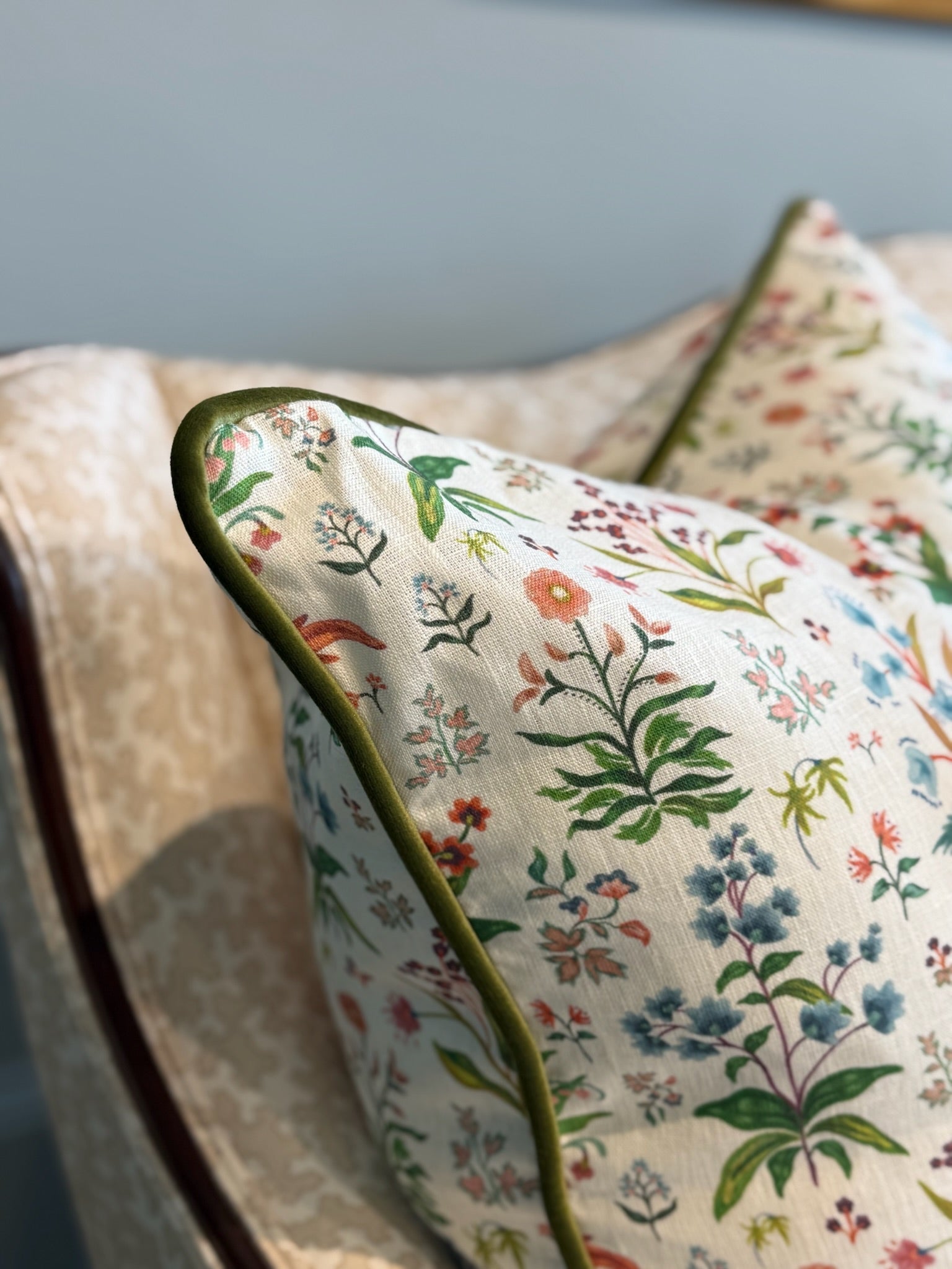 White linen Meadow Multi Pillow with colorful floral print and green piping on a sofa.