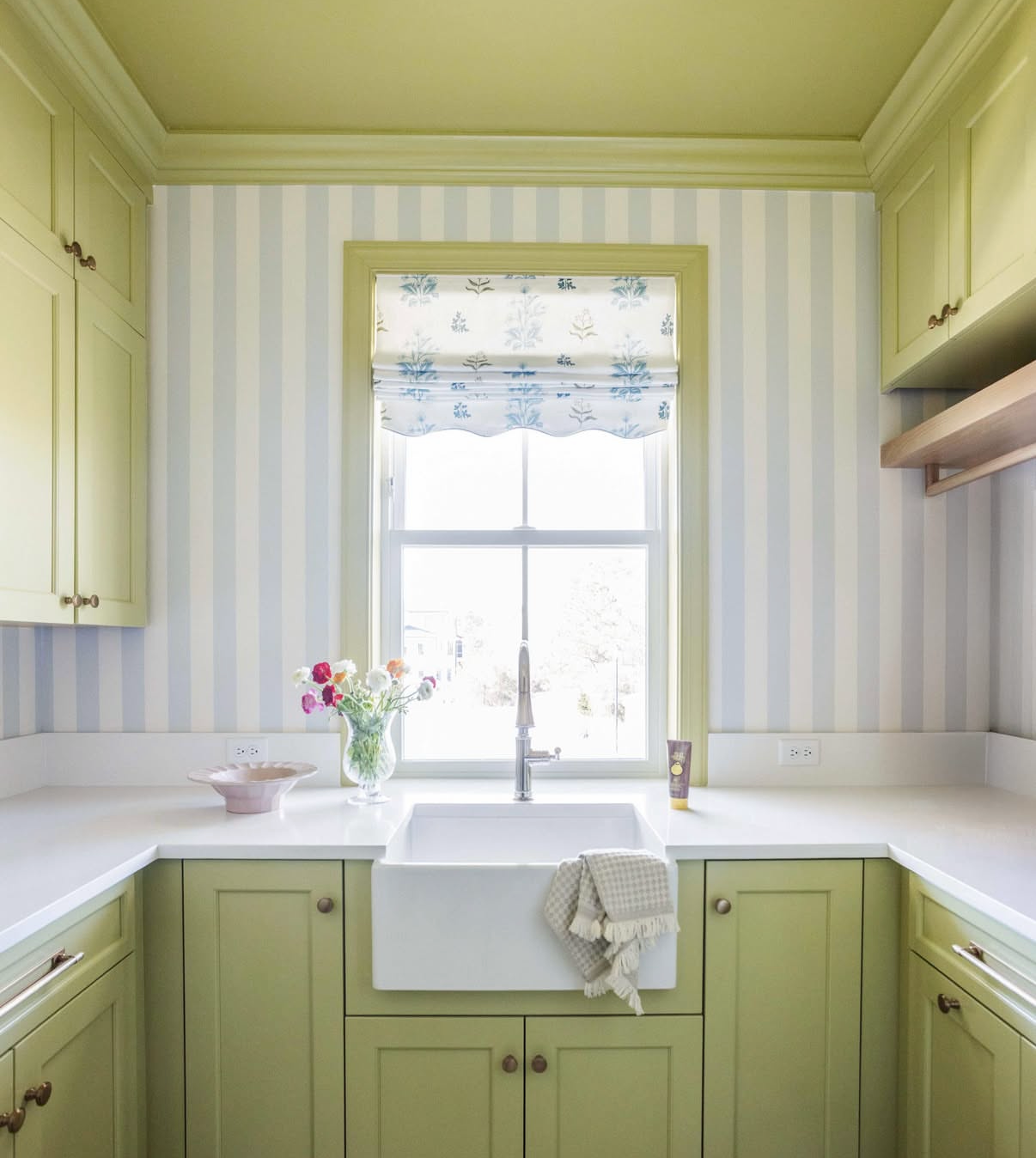 Kitchen with Perennial Fabric "Sprout" roman shade, light green cabinets, and striped wallpaper.
