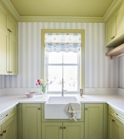 Kitchen with Perennial Fabric "Sprout" roman shade, light green cabinets, and striped wallpaper.