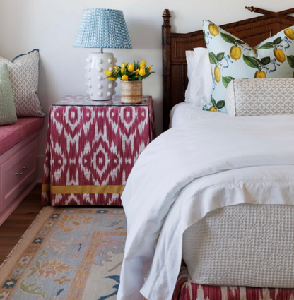 Posey Fabric - Sand, a linen-cotton blend, covers a nightstand in a bedroom with a blue lamp and lemon pillows.