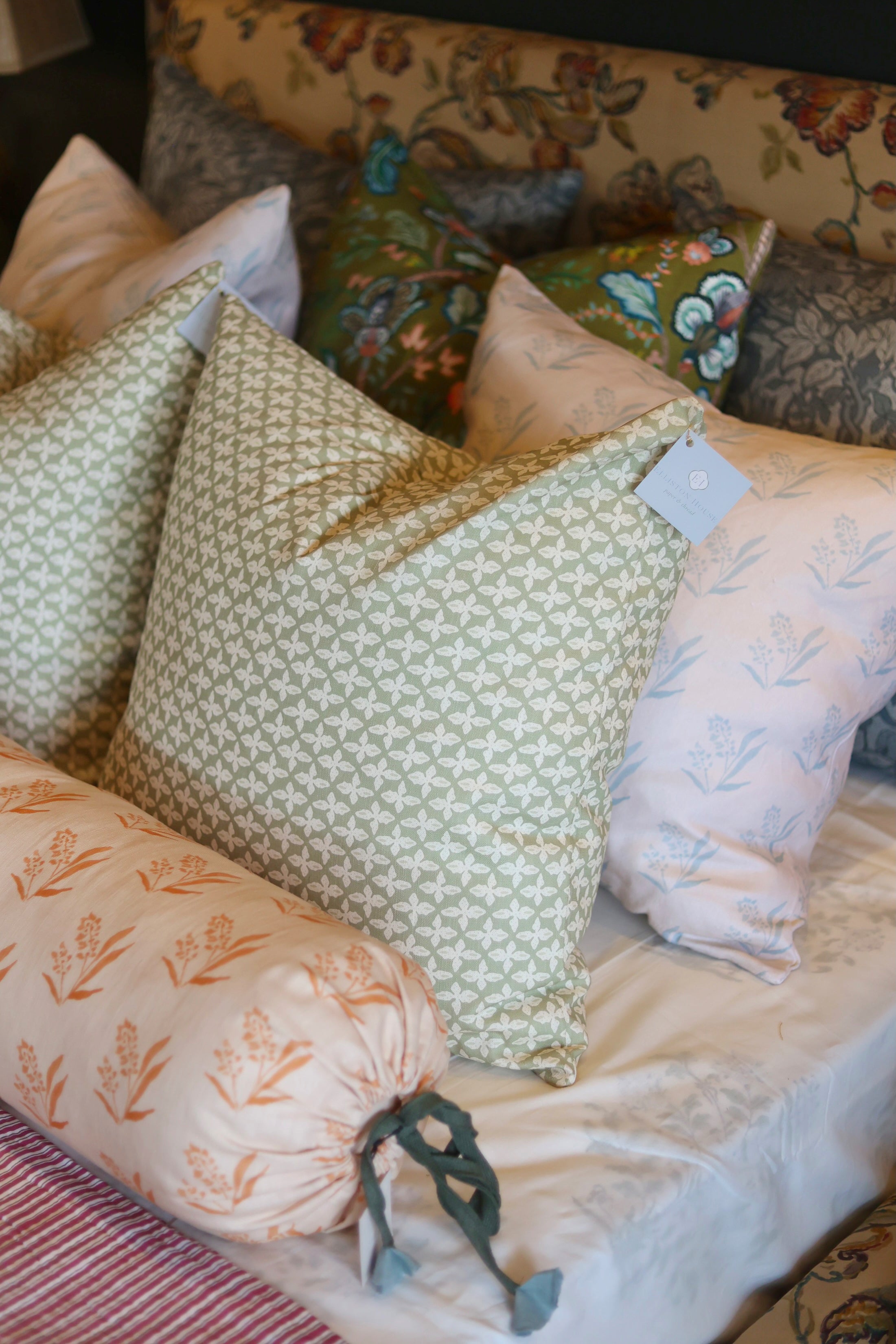 Sage green Posey Fabric pillow with white floral pattern, light pink botanical pillows, and a patterned headboard.