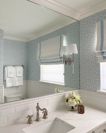 Dover Wallpaper in Pool, a light blue floral pattern, adorns a bathroom wall with white subway tile and vanity.