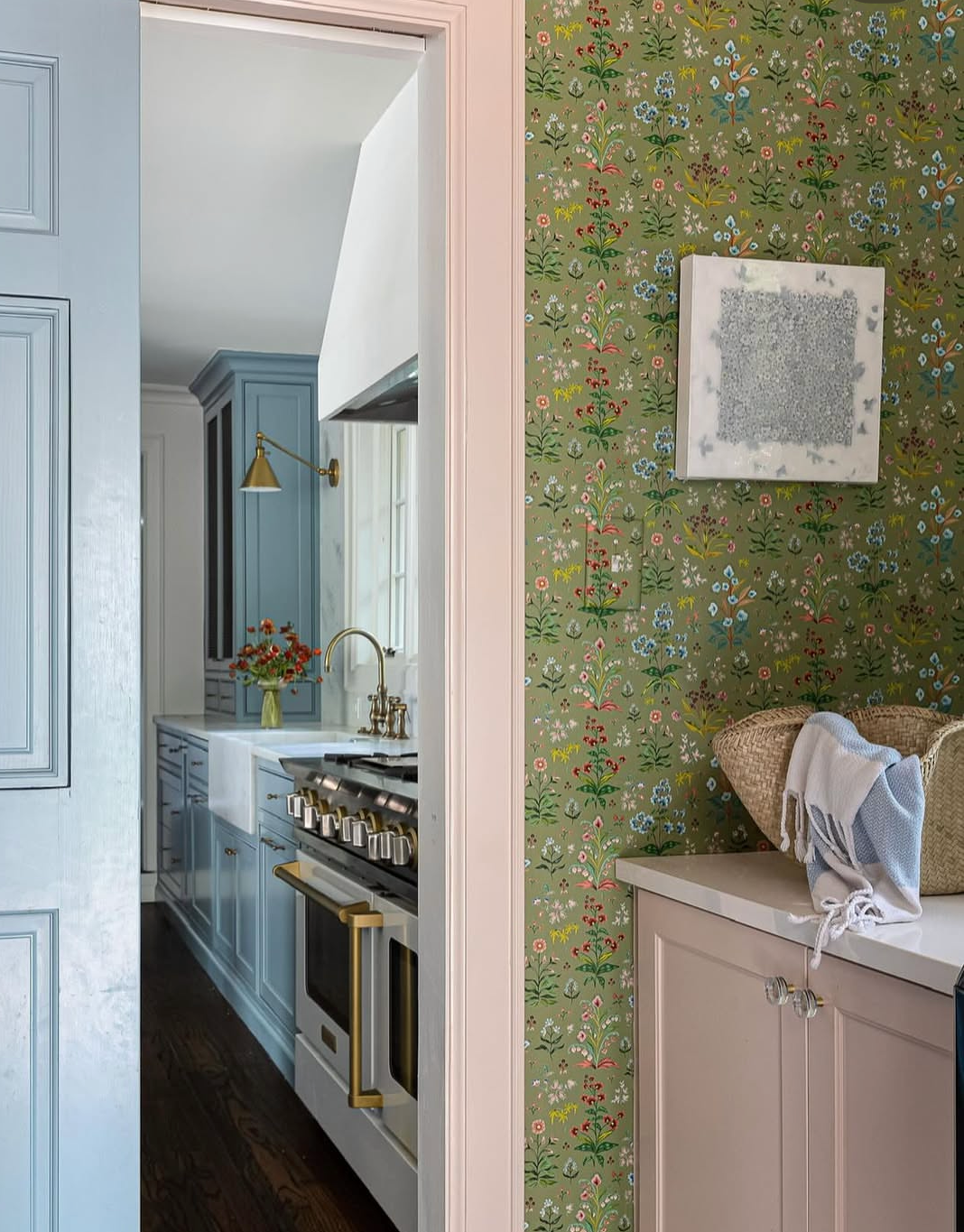 Meadow Multi clay coated wallpaper in House Green with a floral pattern, seen in a room with a light pink cabinet.