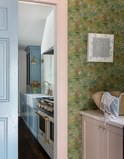 Meadow Multi clay coated wallpaper in House Green with a floral pattern, seen in a room with a light pink cabinet.