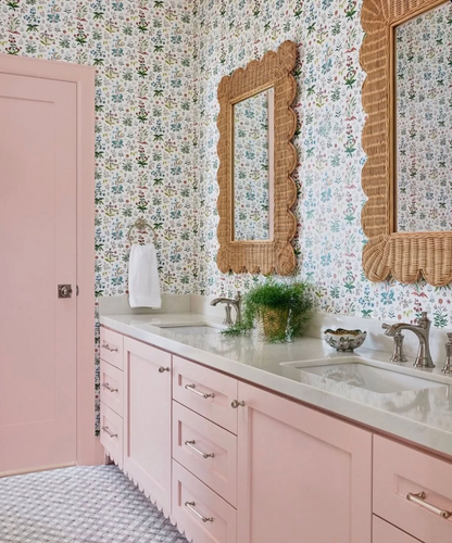 White Meadow Multi clay coated wallpaper with a delicate floral pattern in a bathroom featuring pink vanity and wicker mirrors.