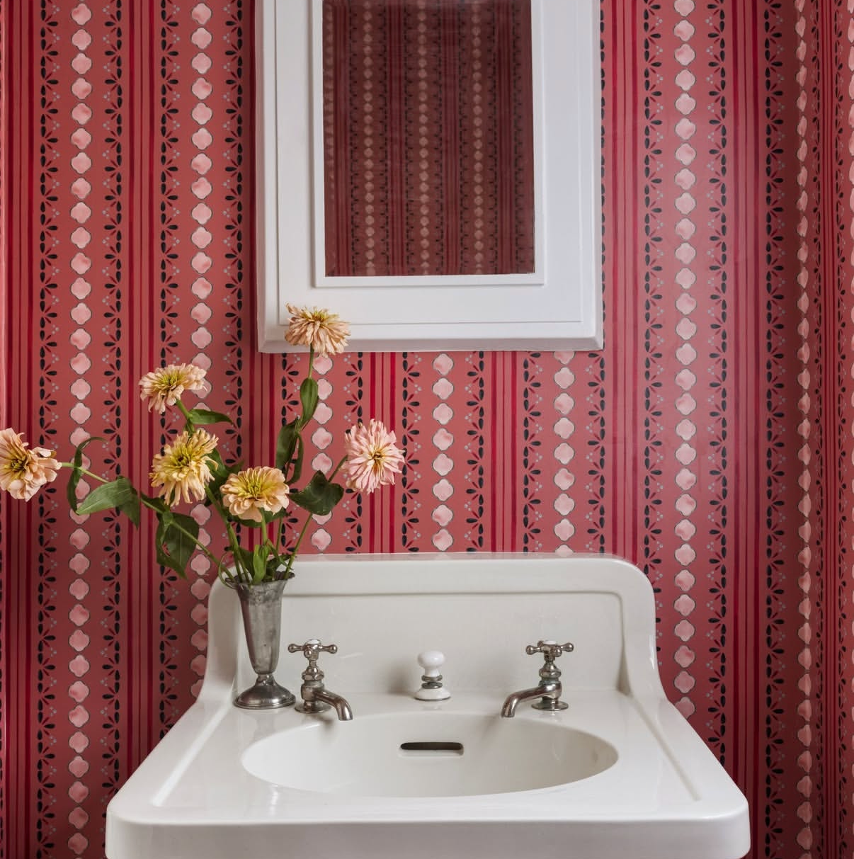 Stratford Petal clay-coated wallpaper with vertical stripes and floral motifs behind a white sink and mirror.