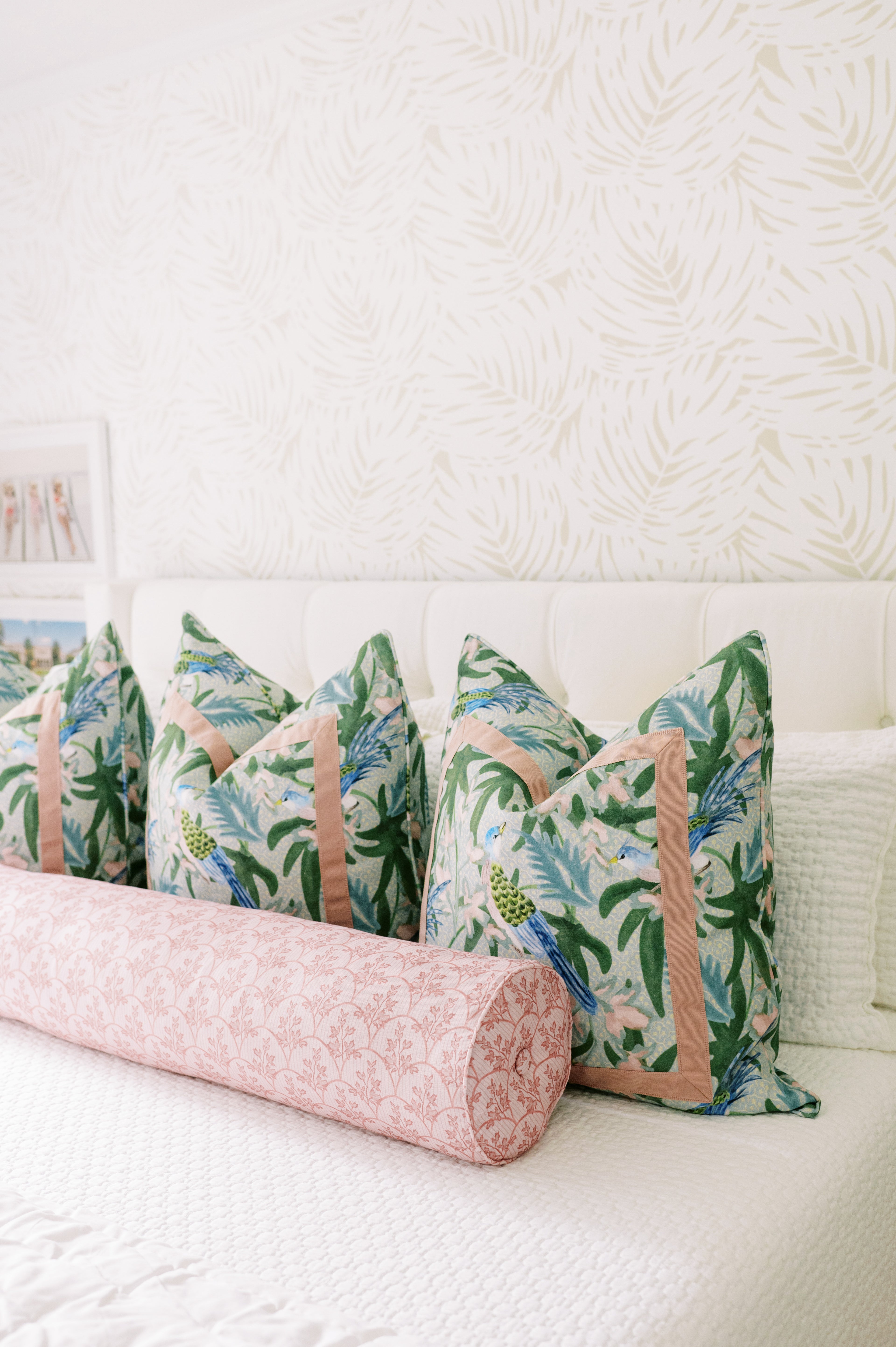 Laurel Fabric - Poppy: linen-cotton blend pillows with tropical birds and foliage, plus a pink patterned bolster.