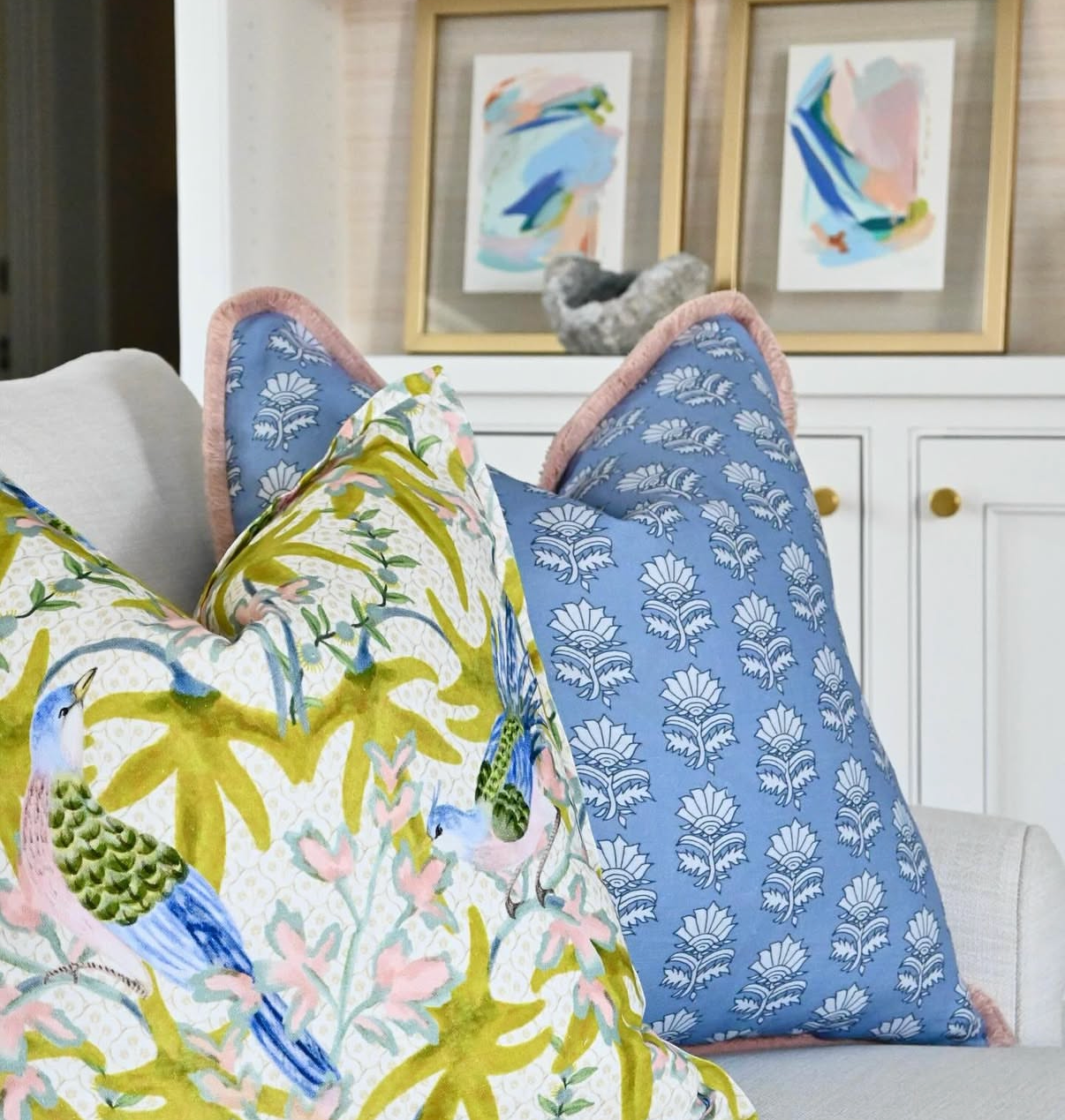 Sparrow Fabric - Citrus Belgian Linen pillow with bird and leaf pattern, next to a blue floral pillow with pink trim.