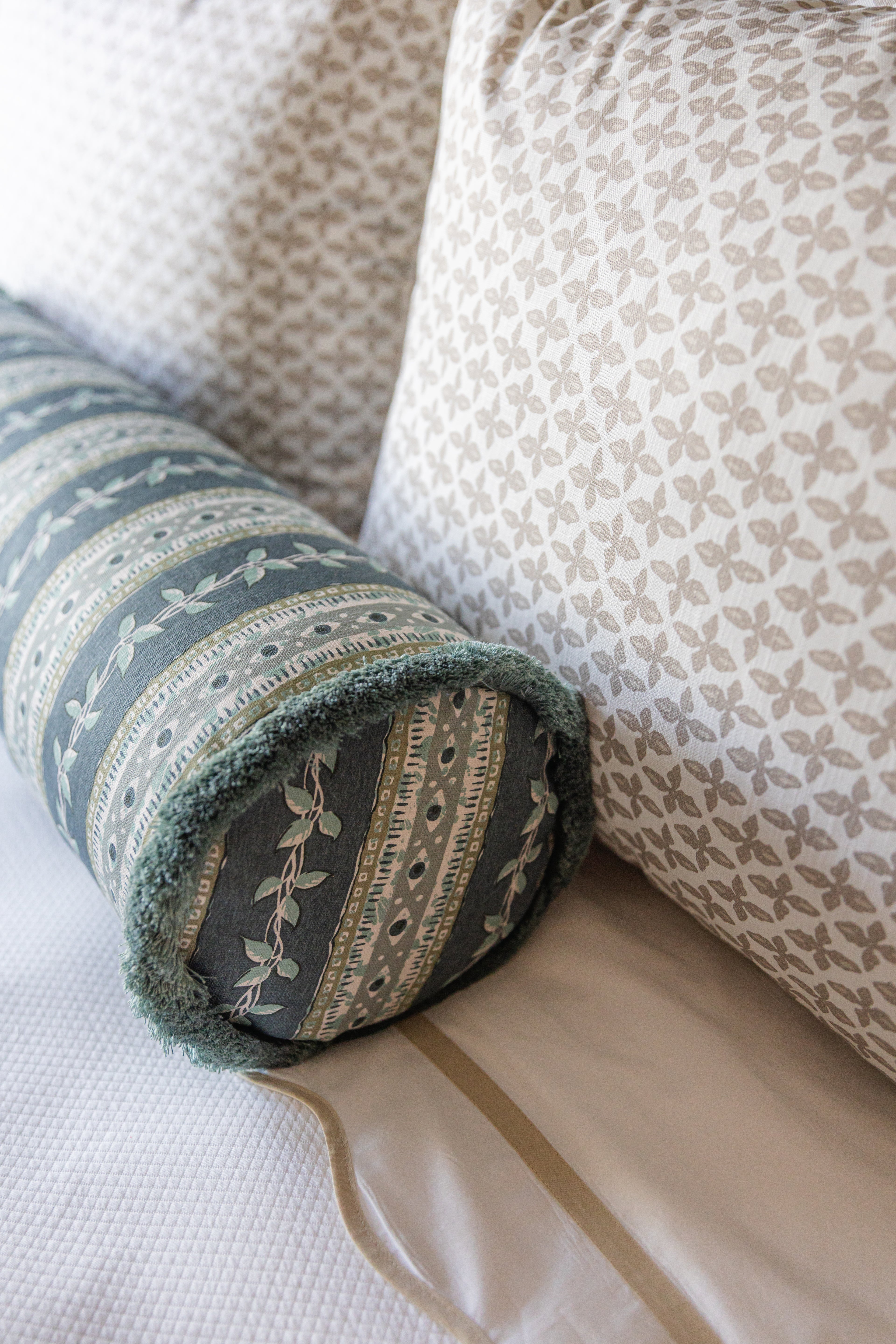 Marine Trellis Fabric bolster pillow with green fringe, alongside a beige patterned pillow.