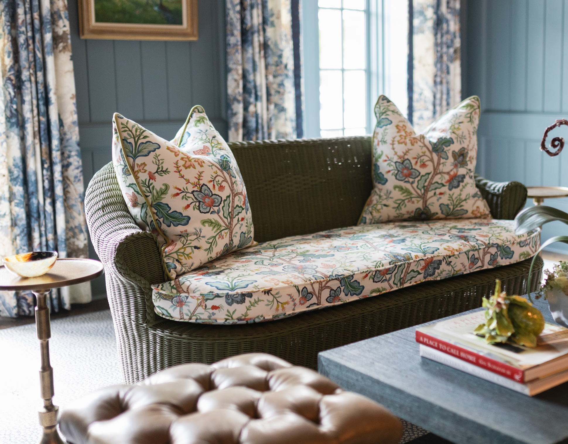 Vera Vine Fabric in white, a floral Belgian linen, on a green wicker sofa with matching pillows.