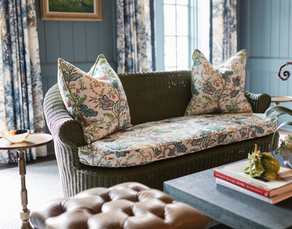 Vera Vine Fabric in white, a floral Belgian linen, on a green wicker sofa with matching pillows.
